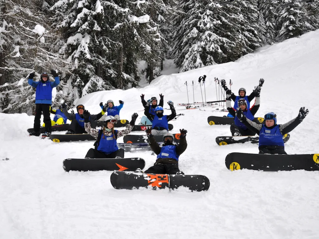 Jugendliche liegen mit Snowboards im Schnee und jubeln.
